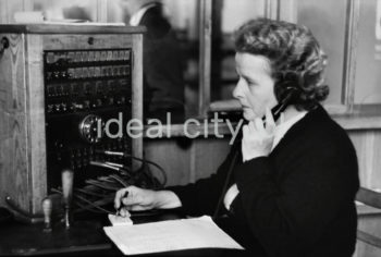 Wnętrze pierwszego urzędu pocztowego w Nowej Hucie, na osiedlu A-1 Północ (Willowe). Poczta została otwarta w połowie 1951 roku. Wystrój wnętrza, m.in. meble, kolumny pokryte marmurową okładziną, marmurowe blaty, zaprojektował Marian Sigmund. Pierwotnie w tym budynku (na piętrze) miał swoją siedzibę również Międzyzwiązkowy Klub Robotniczy. Na parterze znajdowały się punkty przyjęcia klientów, a na piętrze m.in. rozdzielnia oraz mieszkanie służbowe listonosza, który był jednocześnie stróżem. Listonosze dzielili się na miejskich i wiejskich, norma listonosza miejskiego wynosiła 2 tysiące mieszkańców. Na początku pracowało 7 listonoszy. W tle widoczne domy mieszkalne według projektów warszawskiego architekta Franciszka Adamskiego. Koniec lat 50. XXw. 

fot. Wiktor Pental/idealcity.pl

