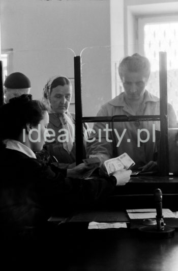 Interior of the first post office in Nowa Huta, A-1 Północ (Willowe) Estate. It opened in mid-1951. The interior, including furniture, columns with marble cladding, and marble tops, was designed by Marian Sigmund. At first, the building also housed the Inter-Union Workers’ Club’s head office (on the first floor). Clients were served on the ground floor, the sorting office and the flat occupied by the postman who was also the caretaker, were located on the first floor. There were urban and rural postmen; an urban postman would visit two thousand people a day. Mid-1950s.

Wnętrze pierwszej poczty w Nowej Hucie na osiedlu A-1 Północ (Willowe). Została ona otwarta w połowie 1951 roku. Wystrój wnętrza, m.in. meble, kolumny pokryte marmurową okładziną, marmurowe blaty, zaprojektował Marian Sigmund. Pierwotnie w tym budynku (na piętrze) miał swoją siedzibę również Międzyzwiązkowy Klub Robotniczy. Na parterze znajdowały się punkty przyjęcia klientów, a na piętrze m.in. rozdzielnia oraz mieszkanie służbowe listonosza, który był jednocześnie stróżem. Listonosze dzielili się na miejskich i wiejskich, norma listonosza miejskiego wynosiła 2 tysiące mieszkańców.
Połowa lat 50. XX w.

Photo by Wiktor Pental/idealcity.pl

