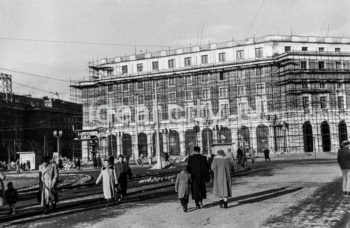 Północna pierzeja Placu Centralnego, widok w kierunku osiedla B-31 (Centrum B) i wylotu alei Lenina (obecnie Solidarności), budynek mieszkalny z lokalami usługowymi na parterze z rusztowaniami podczas tynkowania fasady.  Później od prawej strony, pod arkadami znajdował się na parterze sklep obuwniczy. Projektantem żyrandoli, mebli oraz gablot wystawienniczych był Marian Steczowicz wspólnie z Barbarą Gołajewską. Obok znajdował się sklep z materiałami tekstylnymi „Merino” z wielkimi lustrami, ozdobnymi żyrandolami i masywnymi meblami. Wnętrze zaprojektował Zdzisław Szpyrkowski. Kolejnym lokalem użytkowym był sklep jubilerski z kryształowymi żyrandolami. Projektantem wystroju wnętrza był Czesław Wallis (?). Za nim umiejscowiony był sklep Centrali Przemysłu Ludowego i Artystycznymi „Cepelia”. Na szczególna uwagę zasługiwały w nim: metalowe żyrandole z ręcznie malowanymi elementami ceramicznymi, kolorowe talerze ceramiczne umieszczone w kasetonach oraz uzupełniające całość wystroju wnętrza masywne meble. Elementy i ozdoby ceramiczne wykonała Spółdzielnia rzemiosła Artystycznego „Kamionka” z Łysej Góry, a meble Spółdzielnia Rękodzieła Artystycznego „Meble Artystyczne