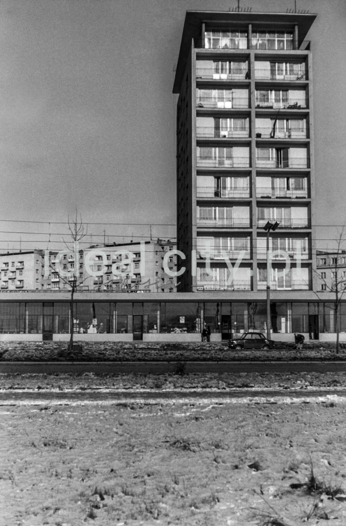 The Centrum D (D-31) Estate, view from Plan 6-letni Alley (Six-Year-Plan Alley; now Jana Pawła II Alley). Block nr 7 (now 8), nicknamed “helicopter,” designed by Kazimierz Chodorowski and Stefan Golonka. It was built in the new “post-thaw” style, close to social realist buildings in Plac Centralny. The ten-storey block was surrounded at the ground level by a glass-walled pavilion housing a variety of shops, including a sweet shop officially called Ciastkarnia Bambo. Apart from flats with big windows and loggias, it held spacious artistic studios. One of the studios was used by Henryk Makarewicz, who took this photograph and also lived there. 1960s.

Osiedle Centrum D (D-31), widok od strony alei Planu 6-letniego (obecnie aleja Jana Pawła II).  Blok nr 7 (obecnie nr 8) czyli tzw. helikopter.. Autorami projektu byli Kazimierz Chodorowski i Stefan Golonka. Został wybudowany w nowej, „poodwilżowej” formie, tuż przy socrealistycznej zabudowie placu Centralnego. Dziesięciopiętrowy punktowiec w poziomie parteru otoczony został pawilonem handlowo-usługowym o szklanej elewacji. Mieściła się w nim m.in.: cukiernia, która oficjalnie zwana była „Ciastkarnią Bambo”. Poza lokalami mieszkalnymi z dużymi oknami i loggiami, posiadał on obszerne pracownie artystyczne. W bloku tym miał pracownie i mieszkał autor fotografii Henryk Makarewicz, l. 60. XX w.

Photo by Henryk Makarewicz/idealcity.pl

