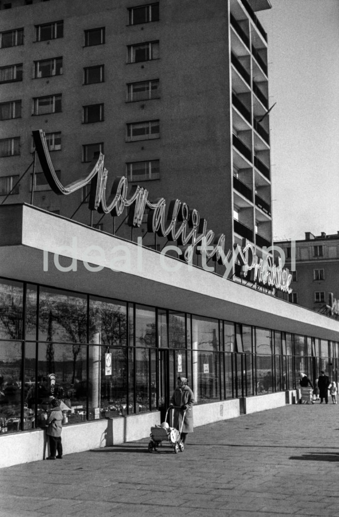 The Centrum D (D-31) Estate, view from Plan 6-letni Alley (Six-Year-Plan Alley; now Jana Pawła II Alley). Block nr 7 (now 8), nicknamed “helicopter,” designed by Kazimierz Chodorowski and Stefan Golonka. It was built in the new “post-thaw” style, close to social realist buildings in Plac Centralny. The ten-storey block was surrounded at the ground level by a glass-walled pavilion housing a variety of shops, including a sweet shop officially called Ciastkarnia Bambo. Apart from flats with big windows and loggias, it held spacious artistic studios. One of the studios was used by Henryk Makarewicz, who took this photograph and also lived there. 1960s.

Osiedle Centrum D (D-31), widok od strony alei Planu 6-letniego (obecnie aleja Jana Pawła II) na pawilon oraz blok mieszkalny.  Blok nr 7 (obecnie nr 8) czyli tzw. helikopter.. Autorami projektu byli Kazimierz Chodorowski i Stefan Golonka. Został wybudowany w nowej, „poodwilżowej” formie, tuż przy socrealistycznej zabudowie placu Centralnego. Dziesięciopiętrowy punktowiec w poziomie parteru otoczony został pawilonem handlowo-usługowym o szklanej elewacji. Mieściła się w nim m.in.: cukiernia, która oficjalnie zwana była „Ciastkarnią Bambo”. Poza lokalami mieszkalnymi z dużymi oknami i loggiami, posiadał on obszerne pracownie artystyczne. W bloku tym miał pracownie i mieszkał autor fotografii Henryk Makarewicz, l. 60. XX w.

Photo by Henryk Makarewicz/idealcity.pl

