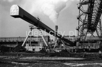 Kombinat metalurgiczny im. Lenina, most przeładunkowy na składowisku surowców z suwnicą bramową z taśmociągiem, lata 60.
Suwnica bramowa składa się z pomostu zawieszonego na dwóch bocznych mostach, wiążących dwie lub więcej bram. Każda z bram wyposażona jest w podwozie typu szynowego lub kołowego. Po pomoście przesuwa się cięgnik.


fot. Henryk Makarewicz/idealcity.pl



