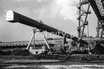 Kombinat metalurgiczny im. Lenina, most przeładunkowy na składowisku surowców z suwnicą bramową z taśmociągiem, lata 60.
Suwnica bramowa składa się z pomostu zawieszonego na dwóch bocznych mostach, wiążących dwie lub więcej bram. Każda z bram wyposażona jest w podwozie typu szynowego lub kołowego. Po pomoście przesuwa się cięgnik.


fot. Henryk Makarewicz/idealcity.pl



