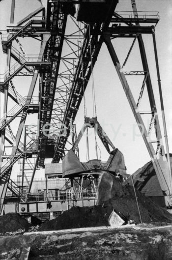 Kombinat metalurgiczny im. Lenina, most przeładunkowy na składowisku surowców z suwnicą bramową z taśmociągiem, lata 60.
Suwnica bramowa składa się z pomostu zawieszonego na dwóch bocznych mostach, wiążących dwie lub więcej bram. Każda z bram wyposażona jest w podwozie typu szynowego lub kołowego. Po pomoście przesuwa się cięgnik.


fot. Henryk Makarewicz/idealcity.pl



