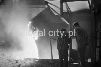 Lenin Metallurgical Combine, inside Converter Plant, drawing a ladle. Second half of the 1960s.
The Converter Plant was opened in February 1966. It was the first steel factory of that kind in Poland. The main building housed the converter hall with two converters, a charging bay and two casting halls. The charge consisted of 70% molten pig iron and about 30% scrap. Molten pig iron came from mixers on torpedo cars holding ladles. Steel was cast into casting ladles placed on a power-driven steel car that crossed casting halls. Once ingot moulds were taken off in their destination hall, ingots were transferred to soaking pits in preparatory rolling mills. Slag was carried to slag disposal sites by slag cars.

Kombinat metalurgiczny im. Lenina, wnętrze hali Stalowni Konwertorowej, wyciąganie kadzi, II połowa lat 60.
Stalownię uruchomiono w lutym 1966 roku. Była pierwszą tego typu stalownią w Polsce. Budynek główny obejmował halę konwerterów z dwoma konwertorami, halę wsadu oraz dwie hale odlewnicze. Wsad metaliczny stanowił 70% płynnej surówki i ok. 30% złomu. Surówka ciekła dostarczana była z mieszalników na surówkowozach, wyposażonych w kadzie. Odlewanie stali odbywało się do kadzi odlewniczych, umieszczonych na napędzanym elektrycznie wozie stalowniczym, jeżdżącym w poprzek hal odlewniczych. Po ściągnięciu wlewnic w odpowiedniej hali, wlewki w stanie gorącym przekazywano do pieców wgłębnych walcowni wstępnych. Żużel wywożono do kafaru na żużlowozach.

Photo by Henryk Makarewicz/idealcity.pl

