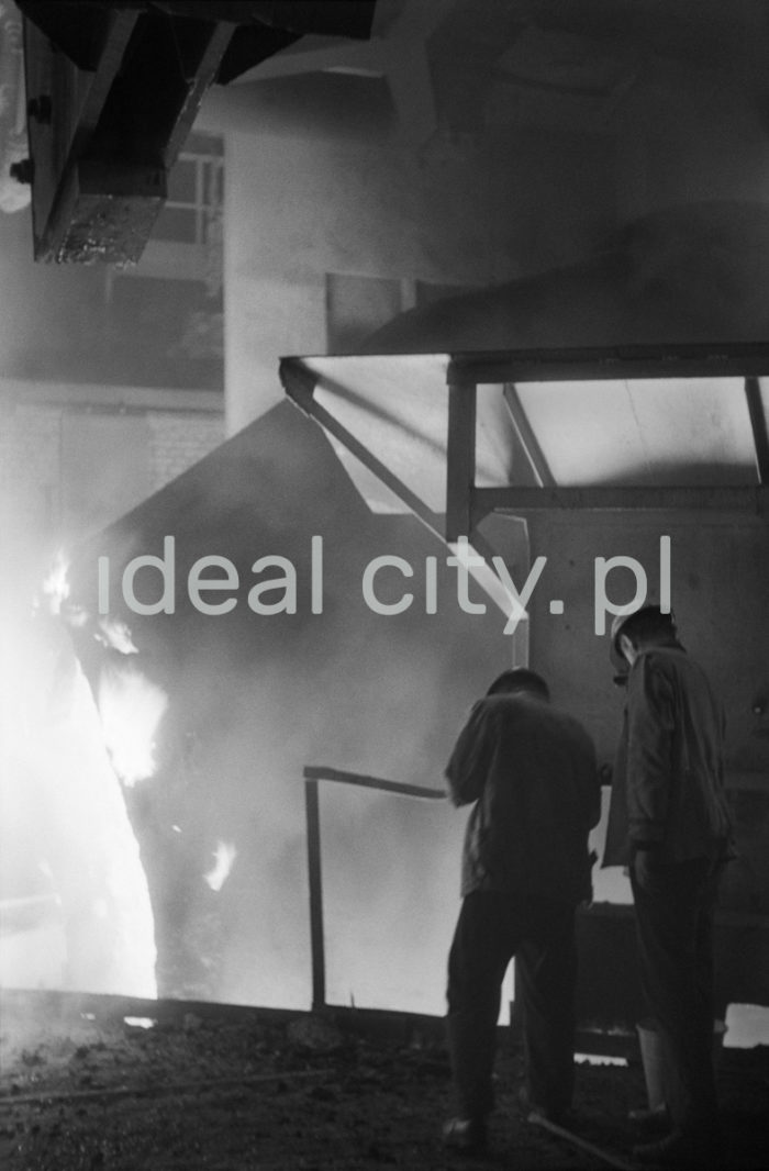 Lenin Metallurgical Combine, inside Converter Plant, drawing a ladle. Second half of the 1960s.
The Converter Plant was opened in February 1966. It was the first steel factory of that kind in Poland. The main building housed the converter hall with two converters, a charging bay and two casting halls. The charge consisted of 70% molten pig iron and about 30% scrap. Molten pig iron came from mixers on torpedo cars holding ladles. Steel was cast into casting ladles placed on a power-driven steel car that crossed casting halls. Once ingot moulds were taken off in their destination hall, ingots were transferred to soaking pits in preparatory rolling mills. Slag was carried to slag disposal sites by slag cars.

Kombinat metalurgiczny im. Lenina, wnętrze hali Stalowni Konwertorowej, wyciąganie kadzi, II połowa lat 60.
Stalownię uruchomiono w lutym 1966 roku. Była pierwszą tego typu stalownią w Polsce. Budynek główny obejmował halę konwerterów z dwoma konwertorami, halę wsadu oraz dwie hale odlewnicze. Wsad metaliczny stanowił 70% płynnej surówki i ok. 30% złomu. Surówka ciekła dostarczana była z mieszalników na surówkowozach, wyposażonych w kadzie. Odlewanie stali odbywało się do kadzi odlewniczych, umieszczonych na napędzanym elektrycznie wozie stalowniczym, jeżdżącym w poprzek hal odlewniczych. Po ściągnięciu wlewnic w odpowiedniej hali, wlewki w stanie gorącym przekazywano do pieców wgłębnych walcowni wstępnych. Żużel wywożono do kafaru na żużlowozach.

Photo by Henryk Makarewicz/idealcity.pl


