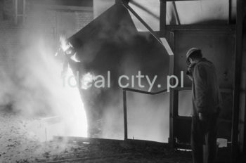 Lenin Metallurgical Combine, inside Converter Plant, drawing a ladle. Second half of the 1960s.
The Converter Plant was opened in February 1966. It was the first steel factory of that kind in Poland. The main building housed the converter hall with two converters, a charging bay and two casting halls. The charge consisted of 70% molten pig iron and about 30% scrap. Molten pig iron came from mixers on torpedo cars holding ladles. Steel was cast into casting ladles placed on a power-driven steel car that crossed casting halls. Once ingot moulds were taken off in their destination hall, ingots were transferred to soaking pits in preparatory rolling mills. Slag was carried to slag disposal sites by slag cars.

Kombinat metalurgiczny im. Lenina, wnętrze hali Stalowni Konwertorowej, wyciąganie kadzi, II połowa lat 60.
Stalownię uruchomiono w lutym 1966 roku. Była pierwszą tego typu stalownią w Polsce. Budynek główny obejmował halę konwerterów z dwoma konwertorami, halę wsadu oraz dwie hale odlewnicze. Wsad metaliczny stanowił 70% płynnej surówki i ok. 30% złomu. Surówka ciekła dostarczana była z mieszalników na surówkowozach, wyposażonych w kadzie. Odlewanie stali odbywało się do kadzi odlewniczych, umieszczonych na napędzanym elektrycznie wozie stalowniczym, jeżdżącym w poprzek hal odlewniczych. Po ściągnięciu wlewnic w odpowiedniej hali, wlewki w stanie gorącym przekazywano do pieców wgłębnych walcowni wstępnych. Żużel wywożono do kafaru na żużlowozach.

Photo by Henryk Makarewicz/idealcity.pl


