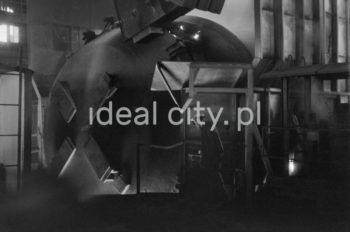 Kombinat metalurgiczny im. Lenina, wnętrze hali Stalowni Konwertorowej, wyciąganie kadzi, II połowa lat 60.
Stalownię uruchomiono w lutym 1966 roku. Była pierwszą tego typu stalownią w Polsce. Budynek główny obejmował halę konwerterów z dwoma konwertorami, halę wsadu oraz dwie hale odlewnicze. Wsad metaliczny stanowił 70% płynnej surówki i ok. 30% złomu. Surówka ciekła dostarczana była z mieszalników na surówkowozach, wyposażonych w kadzie. Odlewanie stali odbywało się do kadzi odlewniczych, umieszczonych na napędzanym elektrycznie wozie stalowniczym, jeżdżącym w poprzek hal odlewniczych. Po ściągnięciu wlewnic w odpowiedniej hali, wlewki w stanie gorącym przekazywano do pieców wgłębnych walcowni wstępnych. Żużel wywożono do kafaru na żużlowozach.

fot. Henryk Makarewicz/idealcity.pl


