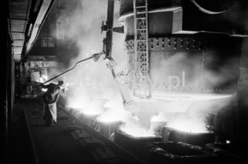 Lenin Metallurgical Combine, inside Converter Plant, pouring steel into ingot moulds. Second half of the 1960s.
The Converter Plant was opened in February 1966. It was the first steel factory of that kind in Poland. The main building housed the converter hall with two converters, a charging bay and two casting halls. The charge consisted of 70% molten pig iron and about 30% scrap. Molten pig iron came from mixers on torpedo cars holding ladles. Steel was cast into casting ladles placed on a power-driven steel car that crossed casting halls. Once ingot moulds were taken off in their destination hall, ingots were transferred to soaking pits in preparatory rolling mills. Slag was carried to slag disposal sites by slag cars.

Kombinat metalurgiczny im. Lenina, wnętrze hali Stalowni Konwertorowej, rozlewanie stali do wlewnic.
Stalownię uruchomiono w lutym 1966 roku. Była pierwszą tego typu stalownią w Polsce. Budynek główny obejmował halę konwerterów z dwoma konwertorami, halę wsadu oraz dwie hale odlewnicze. Wsad metaliczny stanowił 70% płynnej surówki i ok. 30% złomu. Surówka ciekła dostarczana była z mieszalników na surówkowozach, wyposażonych w kadzie. Odlewanie stali odbywało się do kadzi odlewniczych, umieszczonych na napędzanym elektrycznie wozie stalowniczym, jeżdżącym w poprzek hal odlewniczych. Po ściągnięciu wlewnic w odpowiedniej hali, wlewki w stanie gorącym przekazywano do pieców wgłębnych walcowni wstępnych. Żużel wywożono do kafaru na żużlowozach.

Photo by Henryk Makarewicz/idealcity.pl

