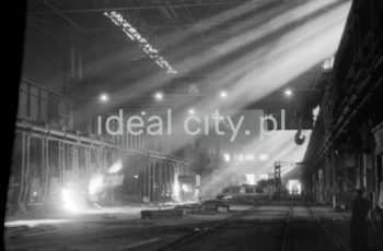Lenin Metallurgical Combine, inside Open Hearth Steel Plant, open hearth furnaces hall, 1960s.
Open Hearth Steel Plant opened in February 1955; the tenth and last furnace was built in 1961. Open hearth furnaces were used for smelting steel from foundry pig iron and steel scrap. Furnaces operated on molten pig iron brought by torpedo ladles from mixers. Steel from furnaces was received from ladles and poured into ingot moulds placed on ingot mould wagons which, appropriately prepared, were steered to the filling hall by railway. Most of the output of open-hearth steel plants was moved to continuous roughers still hot. 1970 saw a modernisation of the Steel Plant, with two old-type furnaces removed. They were replaced by a modern tandem furnace, the first in Poland.

Kombinat metalurgiczny im. Lenina, wnętrze hali Stalowni Martenowskiej, hala pieców martenowskich, lata 60.
Stalownia Martenowska została uruchomiona w lutym 1955 roku, ostatni – dziesiąty piec – wybudowano w 1961 roku. Piece martenowskie używano do wytapiania stali z surówki odlewniczej i złomu stalowego. Piece pracowały przy udziale surówki płynnej, którą pobierano surówkowozami z mieszalników. Stal z pieców odbierana była z kadzi i rozlewana do wlewnic ustawionych na wozach podwlewnicowych, które po odpowiednim przygotowaniu były podstawiane przy pomocy trakcji kolejowej do hali rozlewniczej. Przeważającą większość produkcji stalowni martenowskiej przekazywano do walcowni wstępnych w stanie gorącym. W 1970 roku zmodernizowano Stalownię likwidując dwa piece starego typu. Na ich miejsce wybudowano nowoczesny, pierwszy w Polsce piec typu „tandem”.

Photo by Henryk Makarewicz/idealcity.pl

