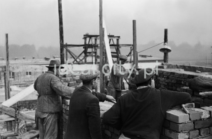 Brygada murarzy przy wznoszeniu domów na Osiedlu Zielonym, w tle Osiedle Sportowe. Budowę najstarszych osiedli rozpoczęto w 23 czerwca 1949 roku właśnie od jej południowo-wschodniej części. Rozpoczęto ją na osiedlach A-1 Północ i A-1 Południe (Willowe i Wandy) oraz A-O (Na Skarpie). Autorami projektu urbanistycznego tych osiedli byli: Tadeusz Ptaszycki, Bolesław Skrzybalski, Adam Fołtyn i Zbigniew Sieradzki. Domy budowano według projektów warszawskiego architekta Franciszka Adamskiego. Były to typowe budynki jedno lub dwupiętrowe z dwuspadowymi dachami z czerwonej dachówki i bez punktów usługowych i biurowych na parterze. Domy Adamskiego wzniesiono również w następnym roku w części osiedla C-2 Północ (Krakowiaków). W przeciwieństwie do domów budowanych na osiedlach A-1 usytuowano je nie w liniach prostych, ale przy wijących się uliczkach. Pierwsze domy rozpoczęto budować bez planów architektonicznych i urbanistycznych nowego miasta, gdyż pracownia projektowa Tadeusza Ptaszyckiego była w studium organizacyjnym i część projektantów przebywała w Warszawie, gdzie utworzono przy Ministerstwie Budownictwa Centralne Biuro Projektów i Studiów Budownictwa Osiedlowego Zakładu Osiedli Robotniczych (CBPiSBO ZOR)  Do biura przy ul. 1 Maja 1 (obecnie ul. biskupa J. Dunajewskiego) w Krakowie wprowadzono się 1 stycznia 1950 roku oficjalnie inaugurując działalność Biura ZOR, 1949 rok.

fot. Wiktor Pental/idealcity.pl

