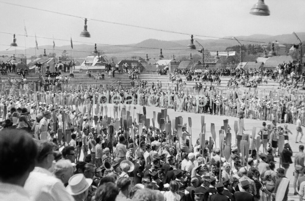 A crowd of canoeists, oars in hand, stand around the open-air stadium.