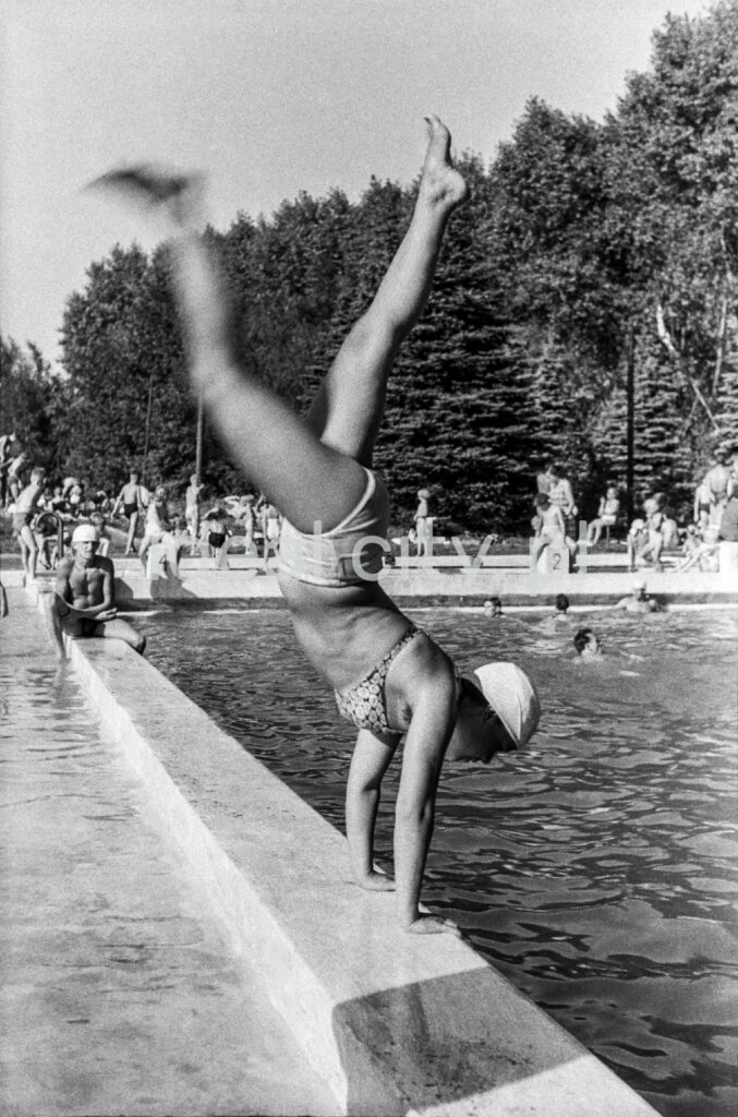 A gymnast in a swimsuit leans back on her hands into the pool.