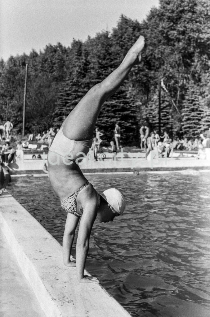 A gymnast in a swimsuit leans back on her hands into the pool.