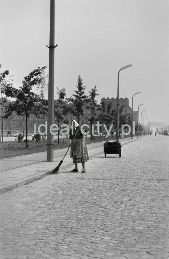 A woman with a broom in her hand and a scarf on her head is sweeping the street.