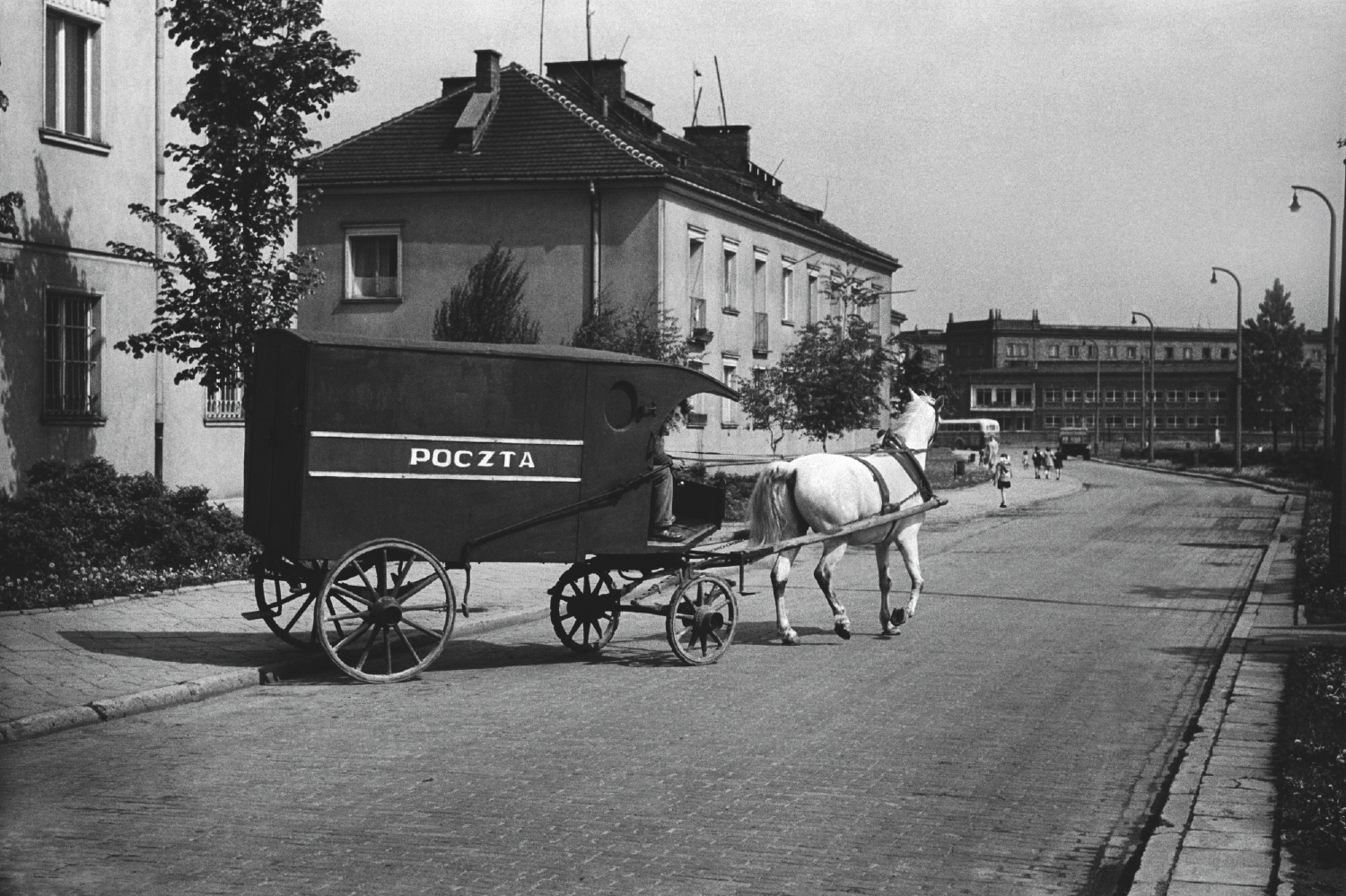 A postal coach drawn by a white horse drives from between the blocks to the street.