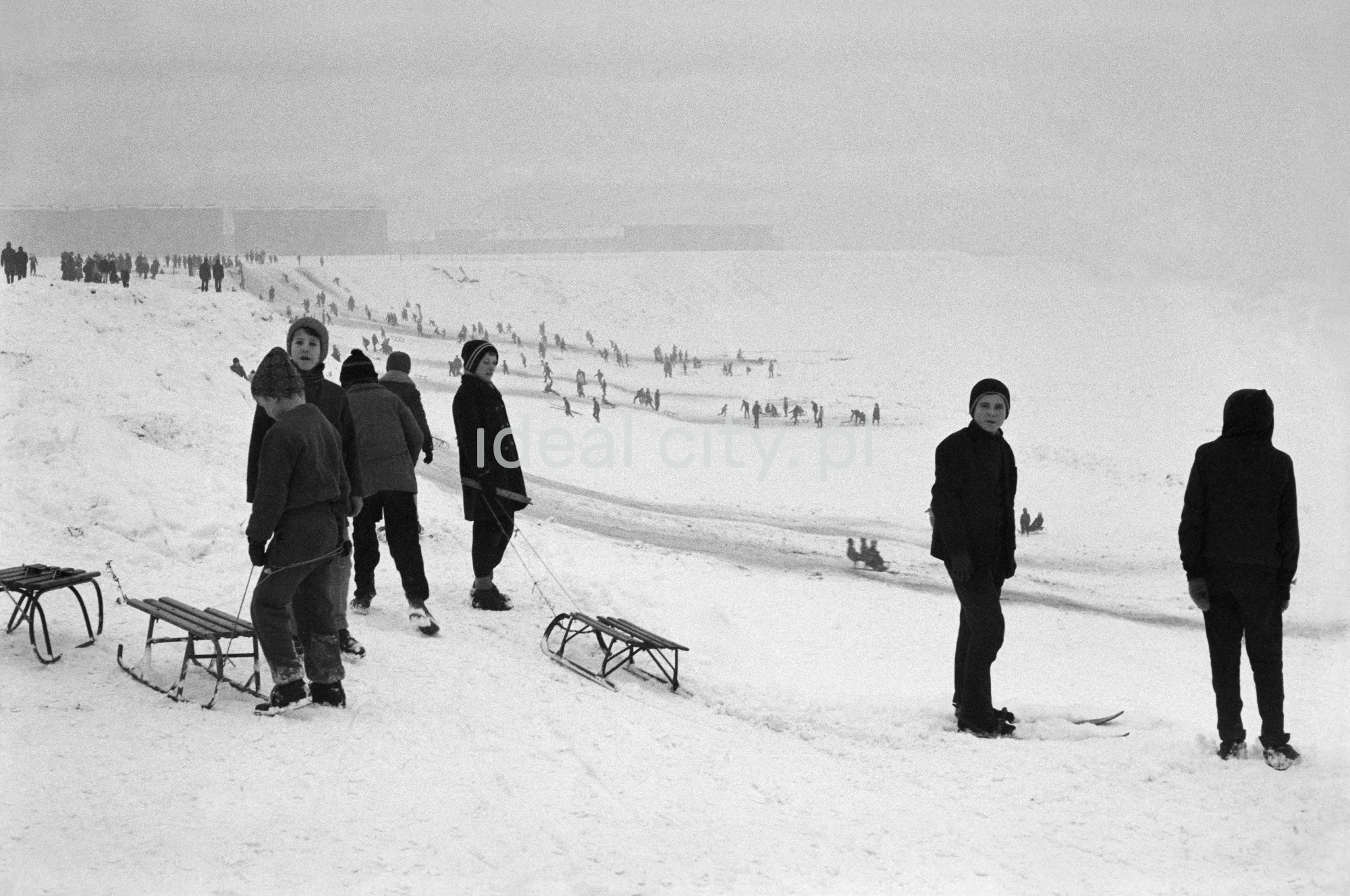 Perspektywiczne ujęcie na tłumy saneczkowiczów na pokrytej śniegiem skarpie.