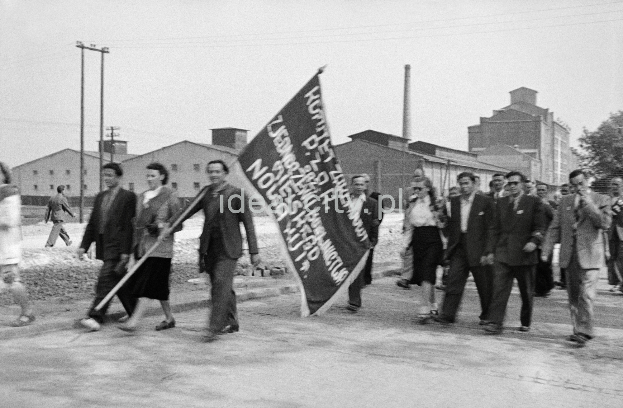 Odświętnie ubrani ludzie maszerują z transparentami.