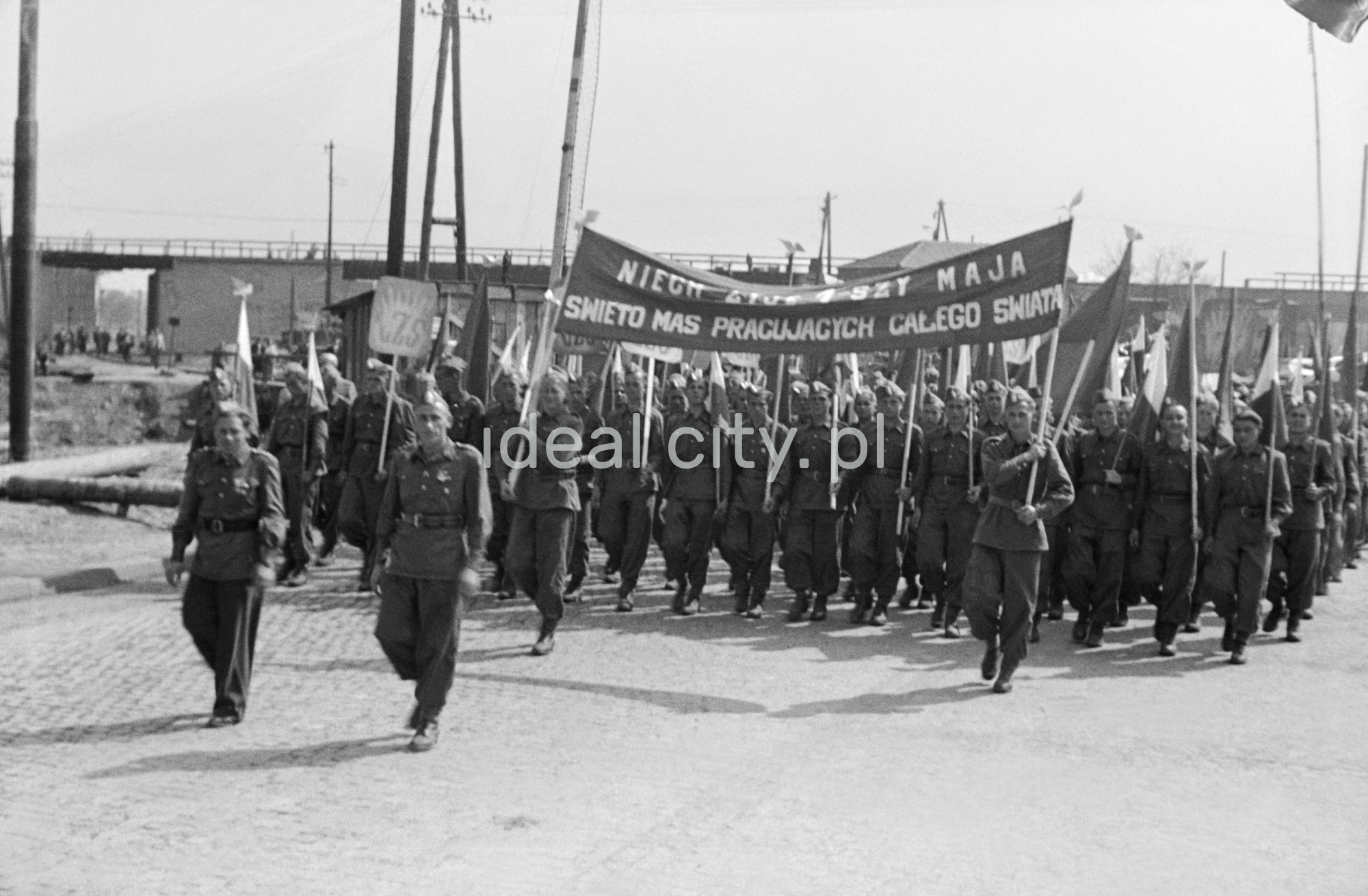 Odświętnie ubrani ludzie maszerują z transparentami.
