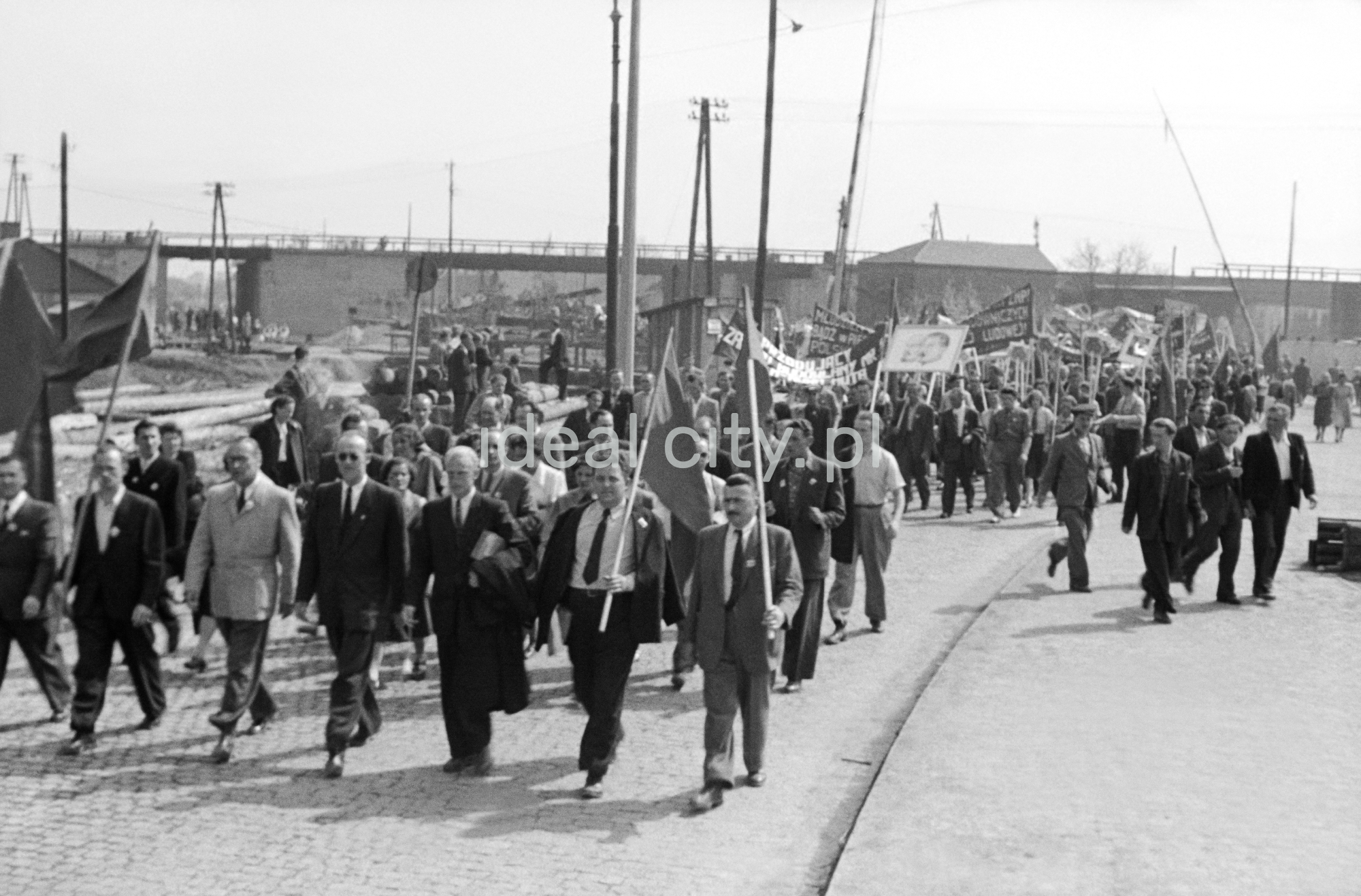 Odświętnie ubrani ludzie maszerują z transparentami.
