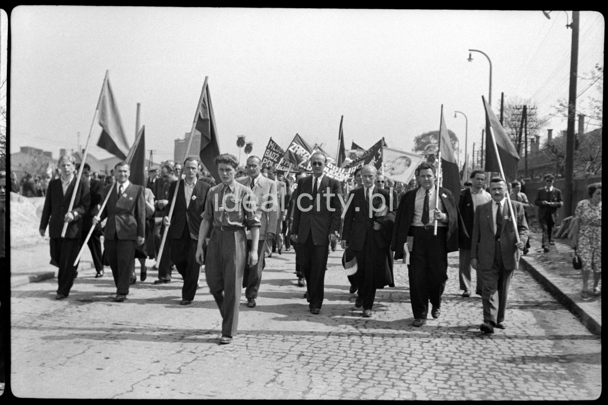 Odświętnie ubrani ludzie maszerują z transparentami.