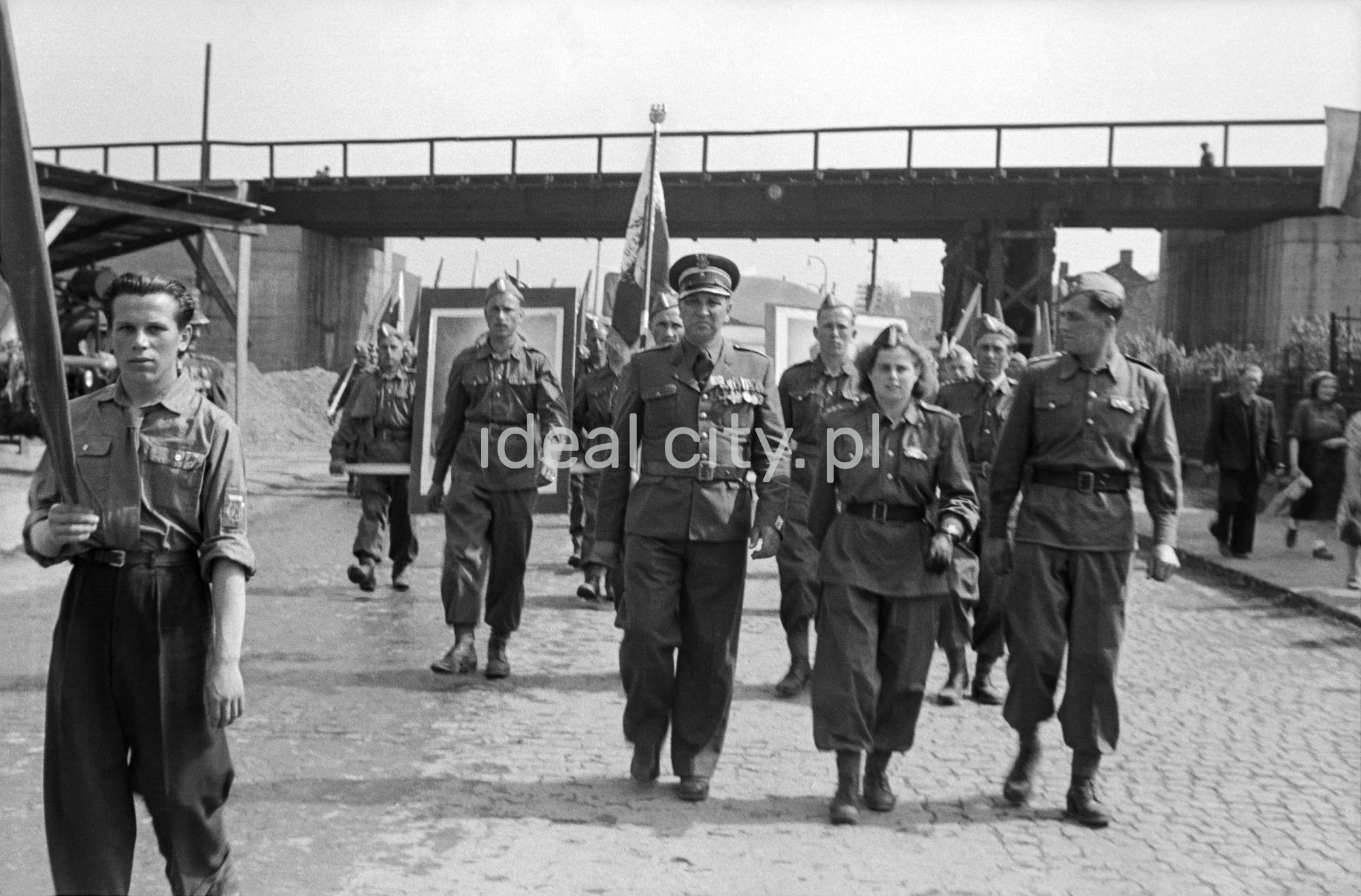 Mężczyźni i kobiety w mundurach maszerują w pochodzie.