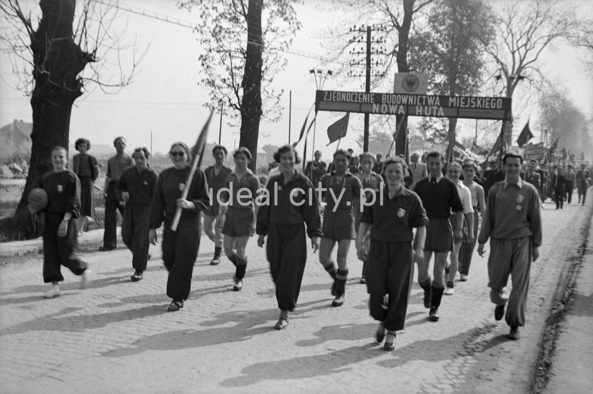 Odświętnie ubrani ludzie maszerują z transparentami.