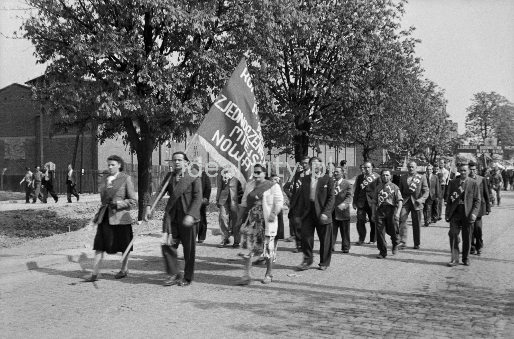 Odświętnie ubrani ludzie maszerują z transparentami.