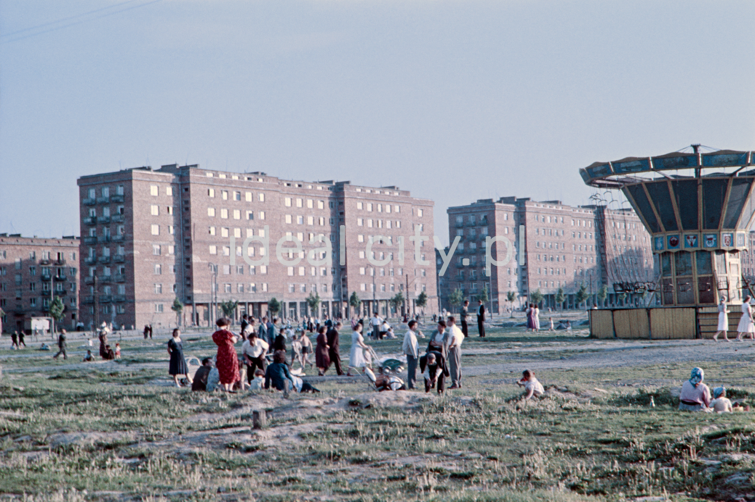 Szerokie ujęcie na bloki i stojącą przed nimi karuzelę.