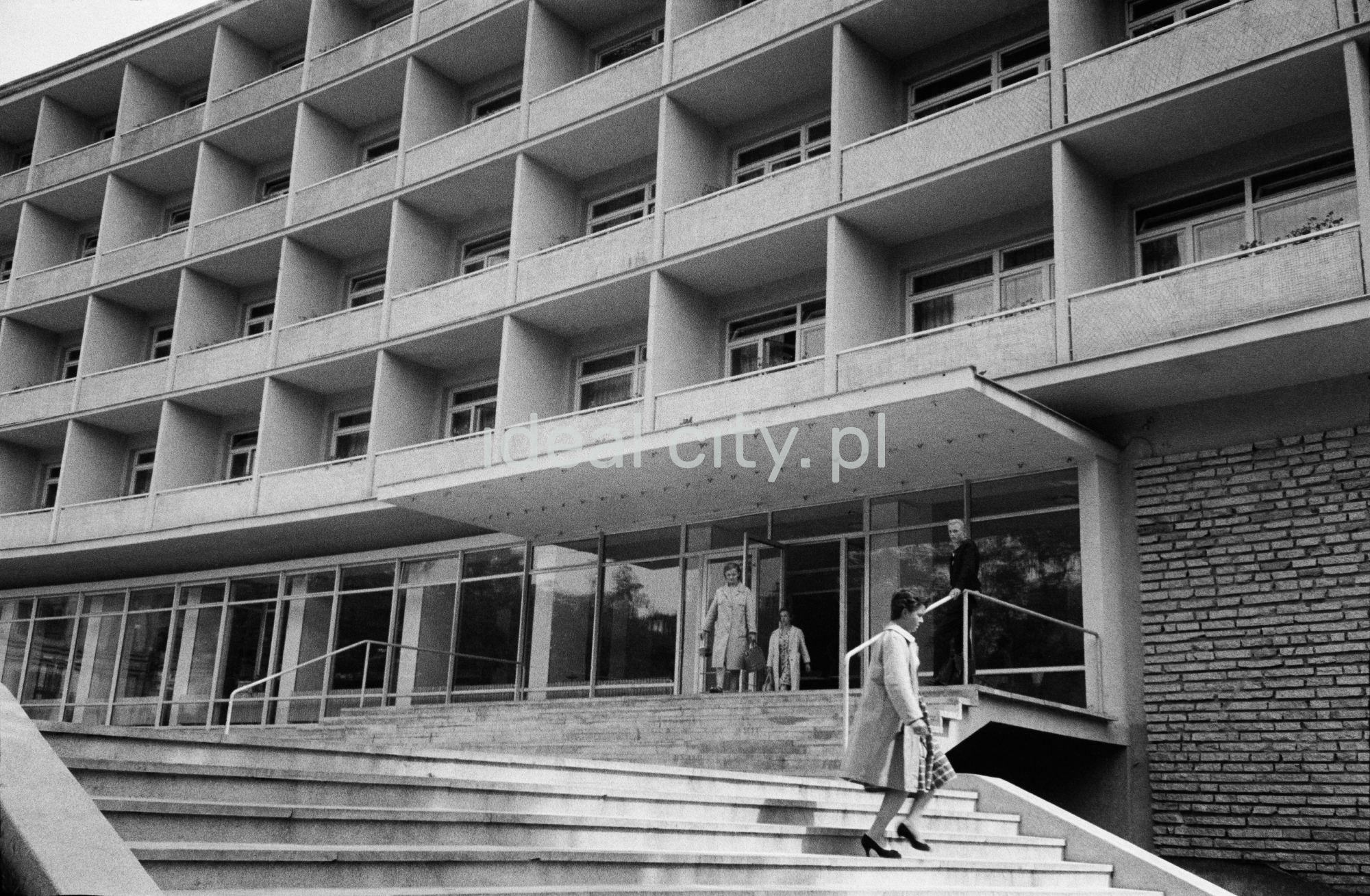 Kobieta schodzi po schodach przed modernistyczną bryłą hotelu.