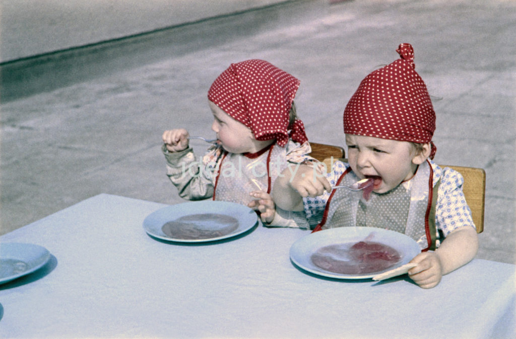 Dzieci w czerwonych hutskach na głowach jedzą zupę z talerzy.