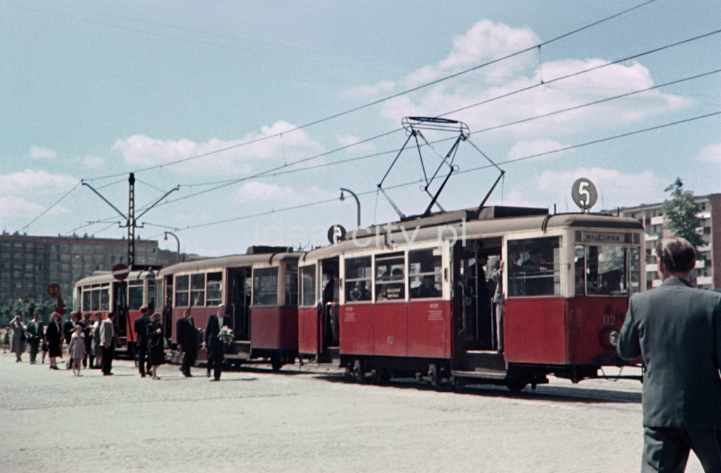 Do biało-czerwonego tramwaju numer pięć wsiadają pasażerowie.